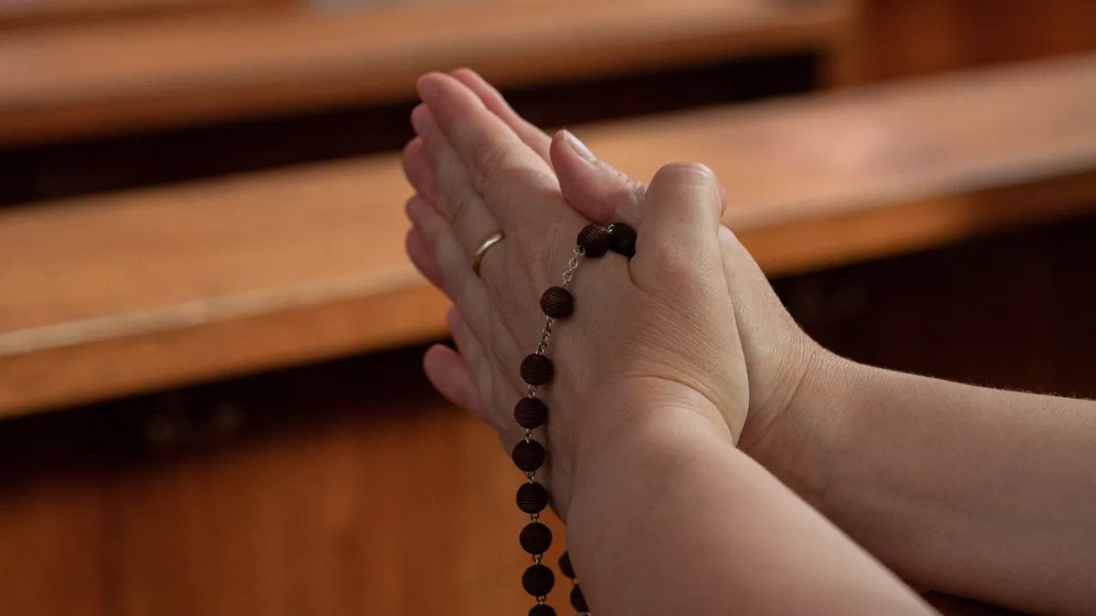 Mãos segurando um terço durante oração em igreja